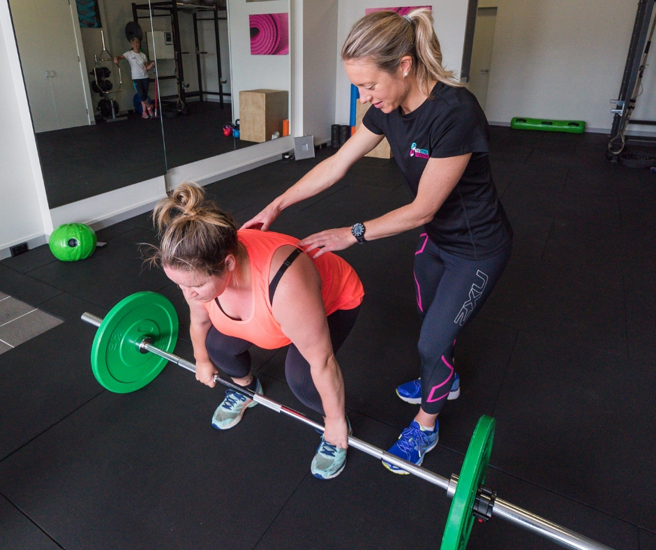 Personal Trainer guiding female client with deadlift
